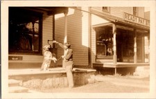 [62k] Postcard RPPC, Man Giving Dog Treat, Street Scene, Stores picture