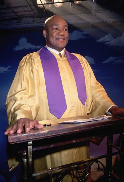 Boxer George Foreman wearing clergy vestments stands at a podium d- Old Photo